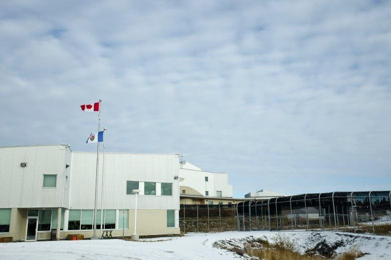 A correctional facility is pictured, with snow on the ground, and flags representing Canada and the Northwest Territories flying above.