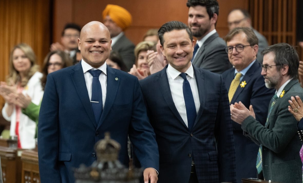 A bald man wearing a blue suit walks down the House of Commons with Pierre Poilievre