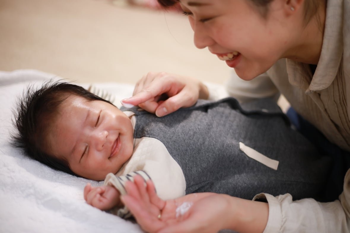 A  mother leans over her new baby while they play.